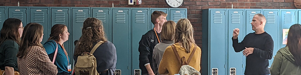 People engaged in an ASL conversation in front of blue lockers in a school hallway.