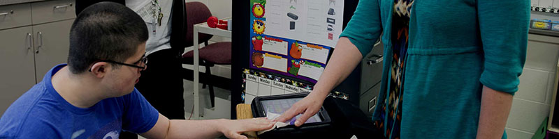 Teacher helping student using a machine for special education learning.