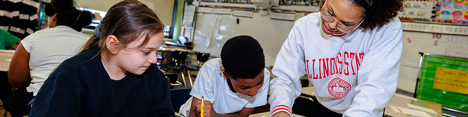 Educational staff helping two students with their assignment.