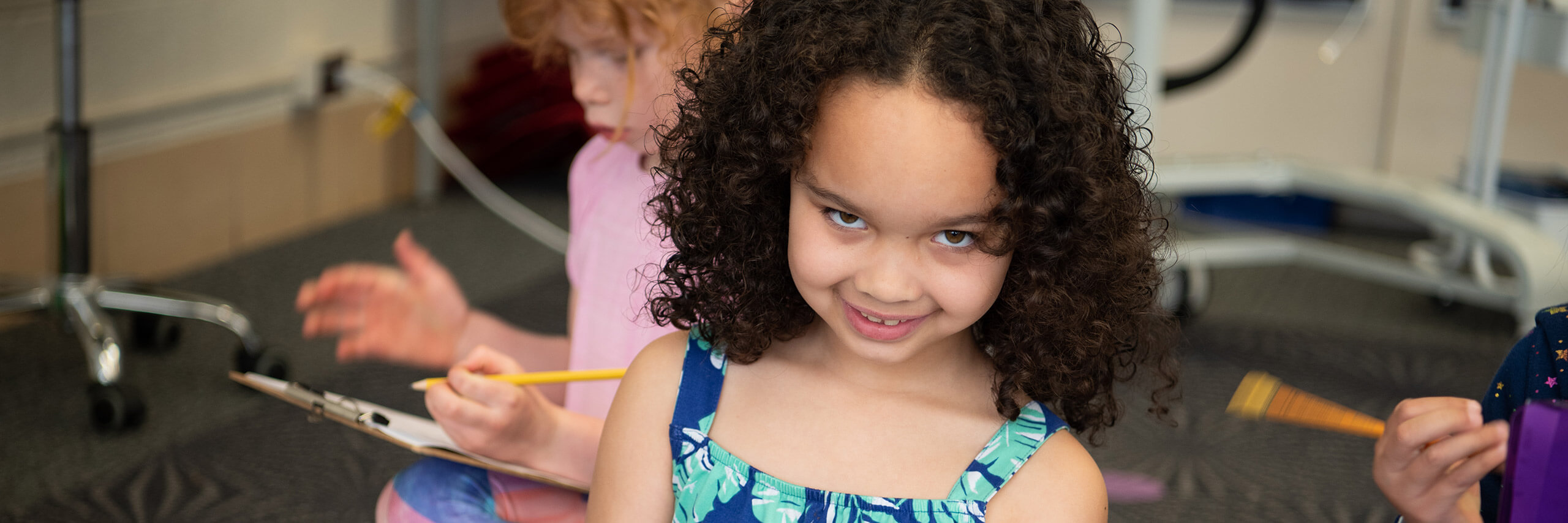 A young girl with curly hair is sitting in a chair, looking content and engaged in her surroundings.