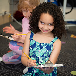 A young girl with curly hair is sitting in a chair, looking content and engaged in her surroundings.