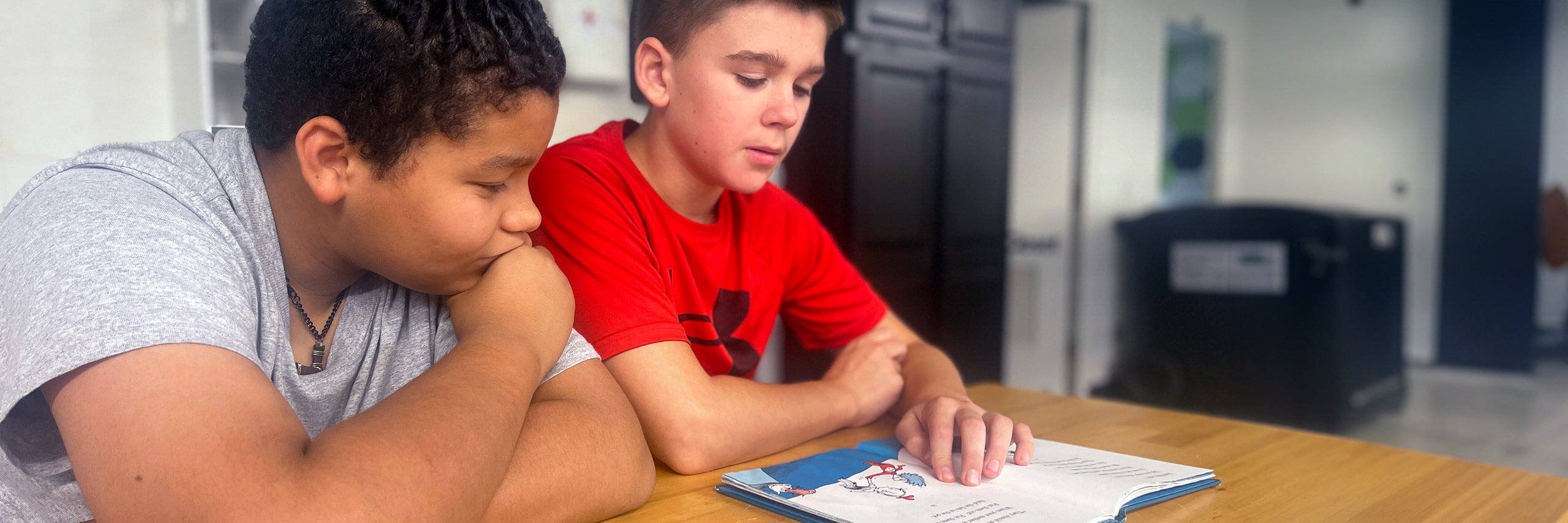 Two boys at a table, focused on a book, illustrating a moment of learning and friendship.