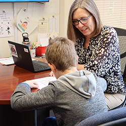 A woman and a child are at a desk with a laptop, illustrating a nurturing educational experience between them.