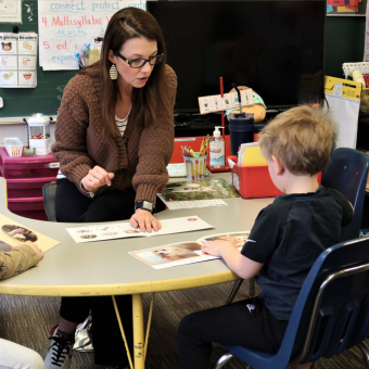 A woman sits with a young boy as he identifies animals in a book