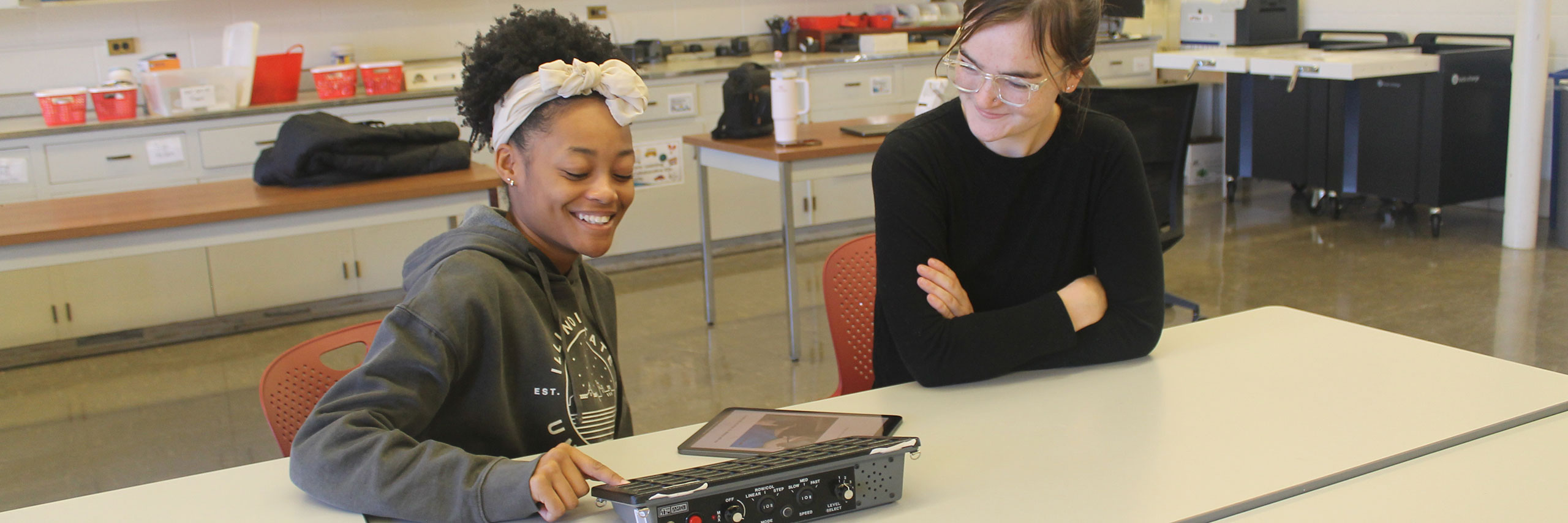 A teacher and a student, seated at a table, working on a project.