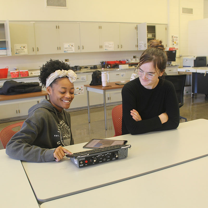 A teacher and a student, seated at a table, working on a project.