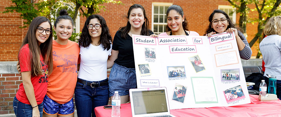 Several college students posing for the camera at the Student Association for Bilingual Education table during Festival ISU.