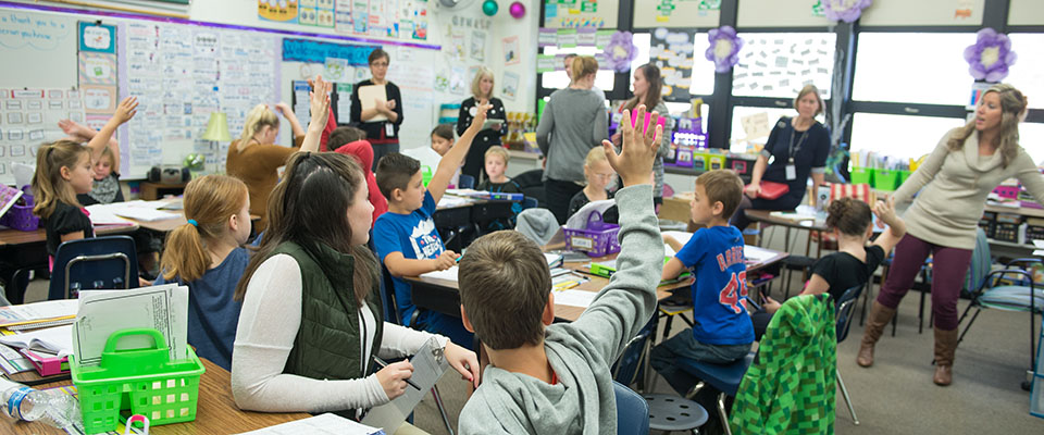 Students in a classroom raising their hands and participating with a group of educators.